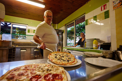 Un chef sert une pizza fraîchement préparée dans la cuisine du Camping Le Coin Tranquille, en Auvergne-Rhône-Alpes.