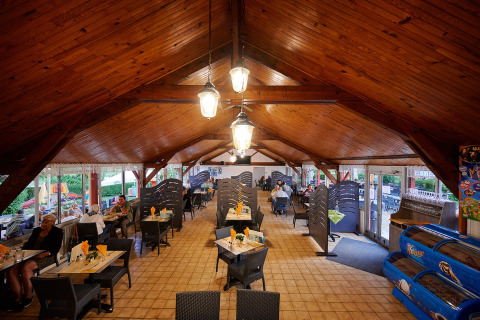 Comedor interior con techo de madera en Camping Le Coin Tranquille, parque vacacional en Auvergne-Rhône-Alpes, Francia.