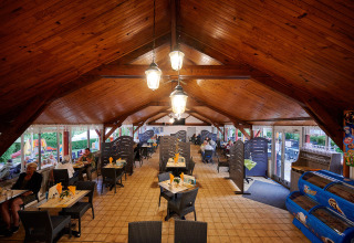 Indendørs spiseområde med træloft og vinduer i Camping Le Coin Tranquille, Auvergne-Rhône-Alpes, Frankrig.