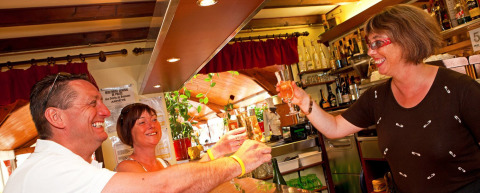Trois adultes souriants trinquent au bar du Camping Le Coin Tranquille en Auvergne-Rhône-Alpes, France.