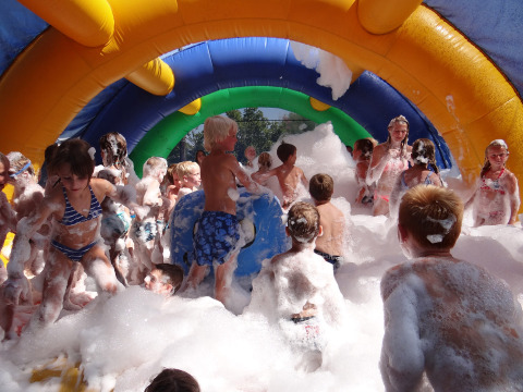 Niños juegan entre espuma bajo un arco inflable colorido en Camping Le Coin Tranquille en Francia.