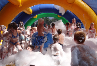 Bambini che giocano nella schiuma sotto un arco gonfiabile colorato a Camping Le Coin Tranquille, Francia.