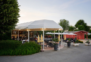 Udendørs restaurantområde med hvide telte og parasoller på Camping Le Coin Tranquille i Frankrig.