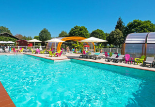 Udendørs swimmingpool med farverige stole og parasoller på Camping Le Coin Tranquille i Frankrig om sommeren.