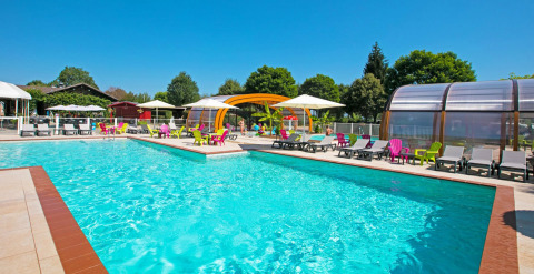 Outdoor swimming pool with colorful loungers and umbrellas at Camping Le Coin Tranquille in France.