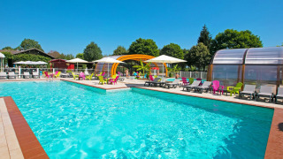 Piscina al aire libre con tumbonas coloridas y sombrillas en Camping Le Coin Tranquille en Francia.