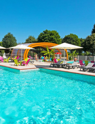 Udendørs swimmingpool med farverige stole og parasoller på Camping Le Coin Tranquille i Frankrig om sommeren.