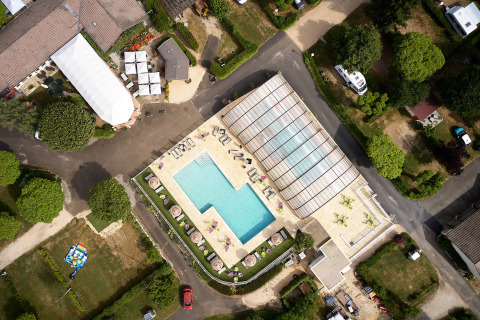 Luftfoto af Camping Le Coin Tranquille med swimmingpool, liggestole og grønne områder i Frankrig.