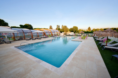 Piscina exterior con tumbonas y sombrillas en Camping Le Coin Tranquille, parque vacacional de Francia.
