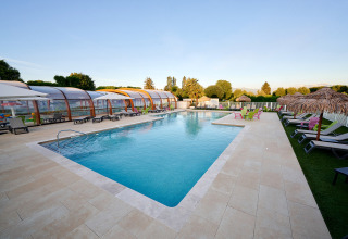 Piscina all'aperto con lettini e ombrelloni al Camping Le Coin Tranquille, parco vacanze in Francia.