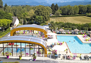 Camping Le Coin Tranquille in Auvergne-Rhône-Alpes con piscine interna ed esterna, lettini e vista sulle montagne.