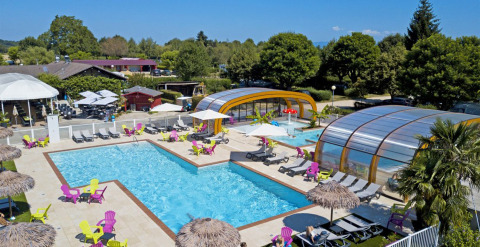 Zona de piscina al aire libre con sillas de colores y piscinas cubiertas en Camping Le Coin Tranquille, Francia.