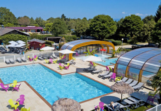 Udendørs swimmingpoolområde med farverige stole og overdækkede bassiner på Camping Le Coin Tranquille i Frankrig.