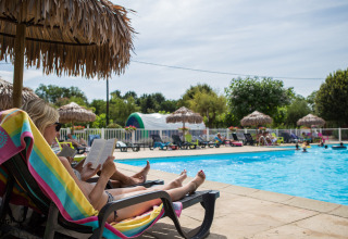 Donna che si rilassa e legge un libro su una sdraio vicino alla piscina al Camping Le Coin Tranquille, Auvergne-Rhône-Alpes.
