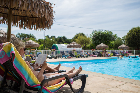 Donna che si rilassa e legge un libro su una sdraio vicino alla piscina al Camping Le Coin Tranquille, Auvergne-Rhône-Alpes.