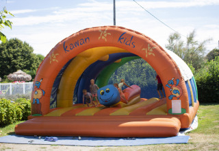 Børn leger på en farverig hoppeborg med teksten 'Kawan Kids' på Camping Le Coin Tranquille i Frankrig.