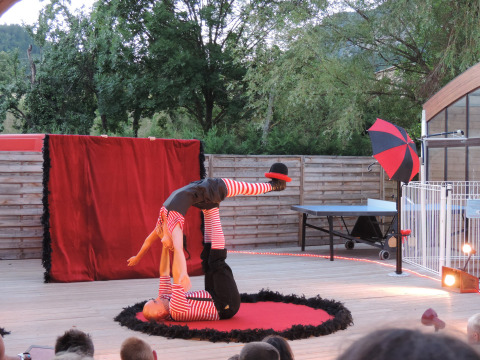 Actuación de circo en Camping Le Lac Bleu con dos acróbatas equilibrándose ante una audiencia al aire libre.