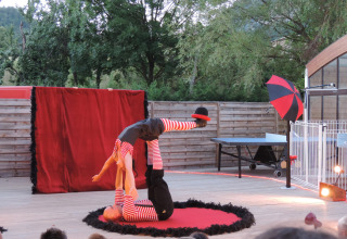 Circusoptreden op Camping Le Lac Bleu, twee acrobaten balanceren op het podium, publiek kijkt toe buiten.