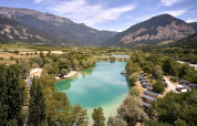Veduta panoramica di Camping Le Lac Bleu in Alvernia-Rodano-Alpi, Francia, con lago, chalet e montagne.