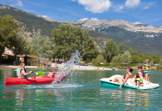 Famiglie si divertono in canoa e pedalò su un lago con vista montagne al Camping Le Lac Bleu, Francia.