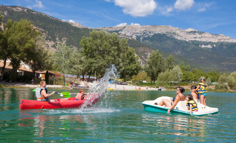 Famiglie si divertono in canoa e pedalò su un lago con vista montagne al Camping Le Lac Bleu, Francia.