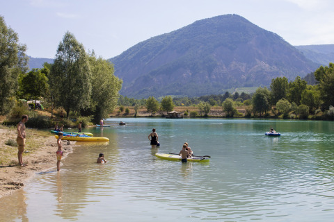Persone che si rilassano e fanno kayak al Camping Le Lac Bleu con le montagne dell’Auvergne-Rhône-Alpes.