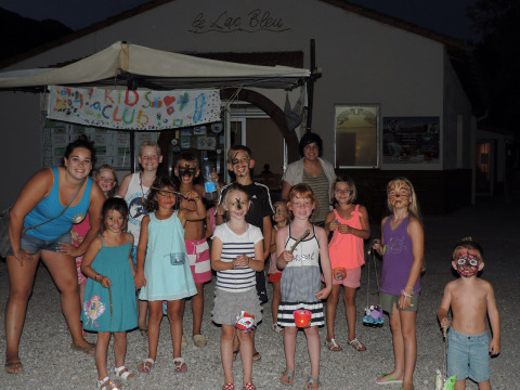 Børn og voksne står foran et skilt med 'Kids Club' på campingpladsen Le Lac Bleu i Auvergne-Rhône-Alpes.