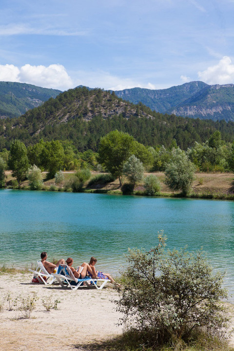 Turisti rilassati su lettini al lago blu con montagne e alberi sullo sfondo in Auvergne-Rhône-Alpes, Francia.