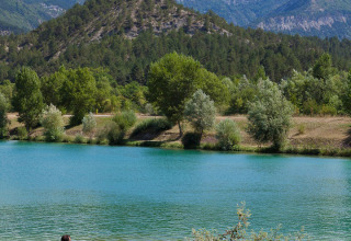 Turisti rilassati su lettini al lago blu con montagne e alberi sullo sfondo in Auvergne-Rhône-Alpes, Francia.