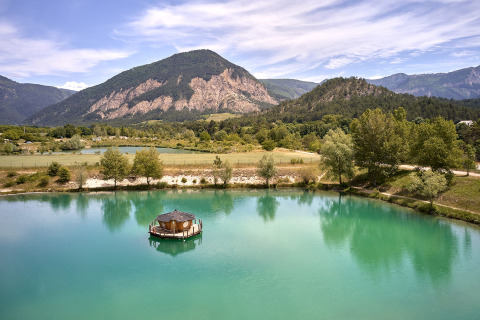 Vista panorámica en Camping Le Lac Bleu en Auvergne-Rhône-Alpes, Francia, con lago y montañas verdes.