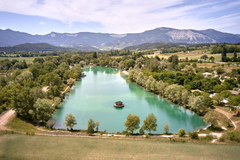 Vista aerea di Camping Le Lac Bleu, parco vacanze con lago e montagne in Auvergne-Rhône-Alpes, Francia.