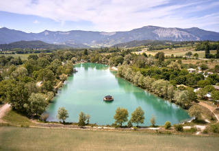 Aerial view of Camping Le Lac Bleu, a holiday park with a scenic lake and mountains in Auvergne-Rhône-Alpes, France.