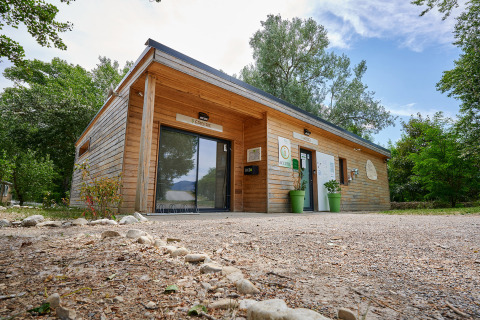 Edificio moderno de madera en Camping Le Lac Bleu, rodeado de árboles en Auvergne-Rhône-Alpes, Francia.