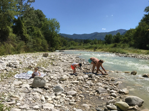 Familia junto al río pedregoso en Camping Le Lac Bleu, rodeada de naturaleza en Auvergne-Rhône-Alpes, Francia.
