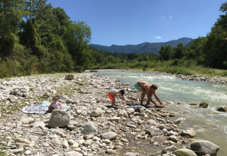 Gezin speelt aan de stenige rivier bij Camping Le Lac Bleu in Auvergne-Rhône-Alpes, Frankrijk.