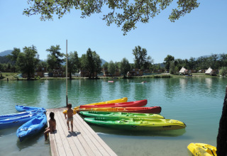 Kinder spielen auf einem Steg mit bunten Kajaks am See im Camping Le Lac Bleu, Auvergne-Rhône-Alpes, Frankreich.