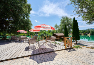 Outdoor seating area with umbrellas by the lake at Camping Le Lac Bleu in Auvergne-Rhône-Alpes, France.