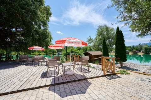 Outdoor seating area with umbrellas by the lake at Camping Le Lac Bleu in Auvergne-Rhône-Alpes, France.