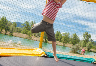 Niño saltando en una cama elástica junto al lago en Camping Le Lac Bleu, parque de vacaciones en Auvernia-Ródano-Alpes, Francia.