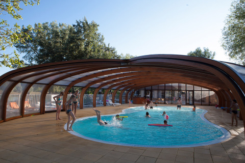 Families enjoy a covered swimming pool at Camping Le Lac Bleu holiday park in Auvergne-Rhône-Alpes, France.