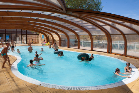 Bambini e adulti nuotano e giocano nella piscina coperta di Camping Le Lac Bleu, Auvergne-Rhône-Alpes, Francia.