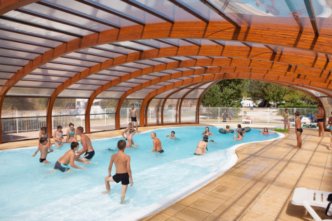 Children and adults play in the covered swimming pool at Camping Le Lac Bleu, a holiday park in Auvergne-Rhône-Alpes.