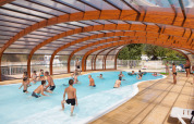 Børn og voksne leger i en overdækket swimmingpool på Camping Le Lac Bleu, en feriepark i Auvergne-Rhône-Alpes.