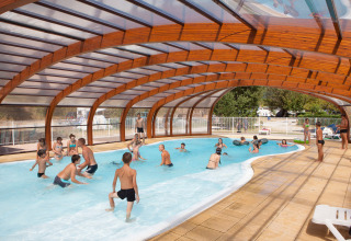 Children and adults play in the covered swimming pool at Camping Le Lac Bleu, a holiday park in Auvergne-Rhône-Alpes.