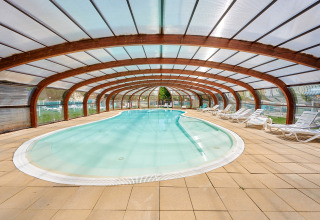 Heated indoor swimming pool with transparent roof and sun loungers at Camping Le Lac Bleu, Auvergne-Rhône-Alpes.