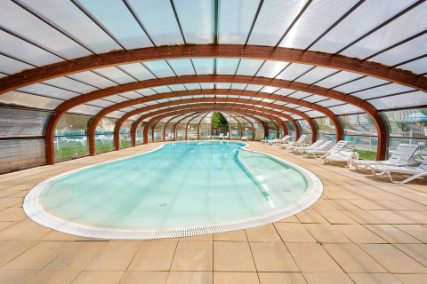 Heated indoor swimming pool with transparent roof and sun loungers at Camping Le Lac Bleu, Auvergne-Rhône-Alpes.