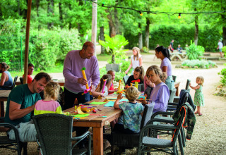 Kinderen en volwassenen knutselen samen buiten aan een tafel op Camping Le Pech Charmant, Frankrijk.