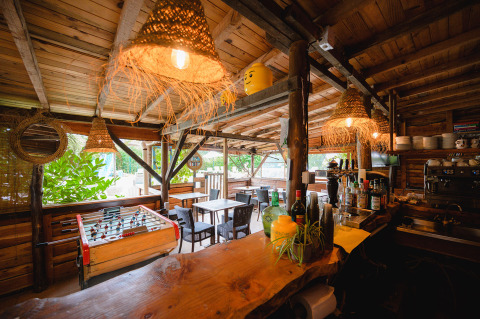 Bar rústico al aire libre con muebles de madera, futbolín y luces acogedoras en Camping Le Pech Charmant.