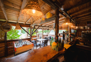 Rustic outdoor bar with wooden furniture, foosball, and cozy lights at Camping Le Pech Charmant in France.