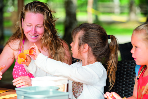 Een vrouw en twee kinderen doen buiten knutselwerkjes op Camping Le Pech Charmant in Nouvelle-Aquitaine, Frankrijk.